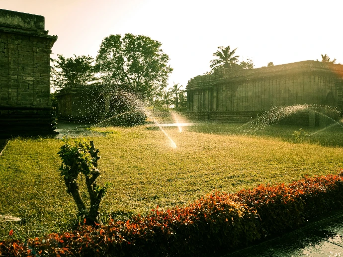 Sprinklers watering a grassy area near old buildings.